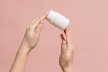 White bottle (plastic tube) in hands on pink background. Packaging for vitamins, pill or capsule, or supplement. Mockup for product branding - obrazy, fototapety, plakaty