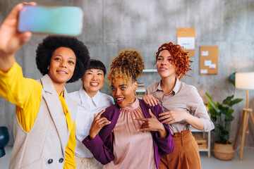Four young business women having fun in office while taking selfies together.