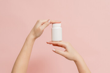 Plastic bottle (tube) in hands on pink background. Packaging for vitamins, tablets or capsule, or...