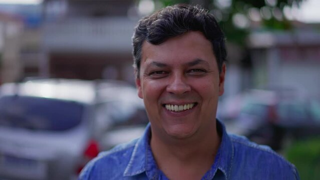 Portrait of a happy diverse Brazilian man standing outside in city street looking at camera smiling. A friendly male person