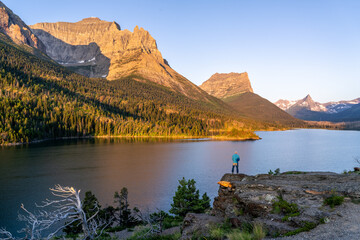 Man standing on a rock cliff looking at a scene of a lake and rugged mountains in the background, Sun Point, St Mary Lake, Glacier National Park, Montana