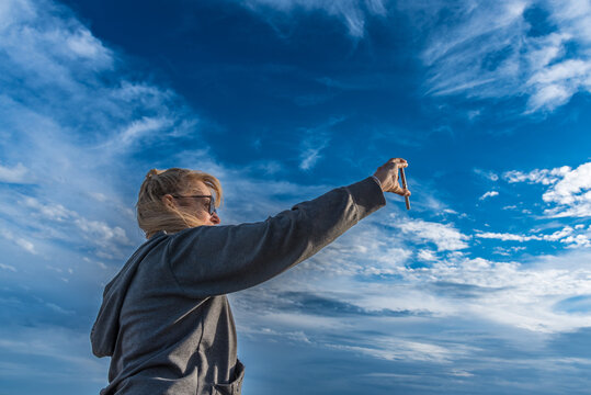 Woman taking selfies with mobile phone outdoors with cloudy blue sky. Technology concept.