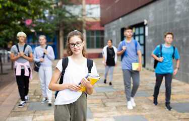 Attractive teenage girl with backpack and workbooks walking to college campus in autumn day.