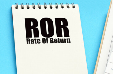 ROR - Rate Of Return words in office notebook next to calculator and calendar.