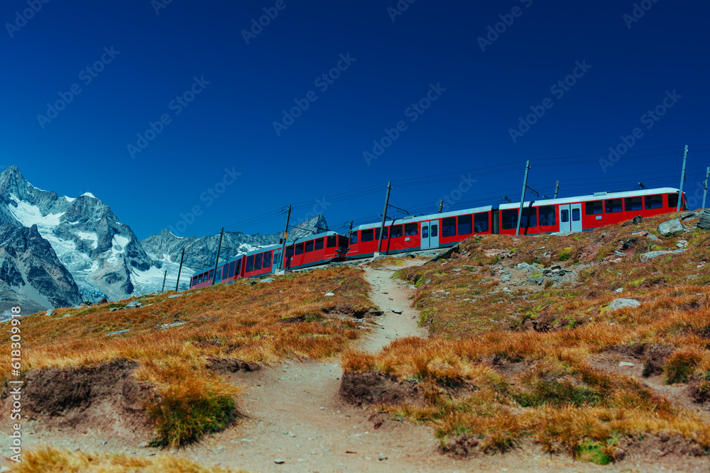 Fototapete Red train in high Alps mountains