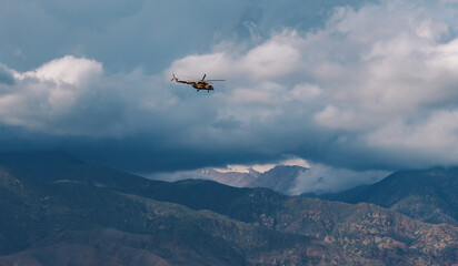 Military helicopter in the sky over the mountains in cloudy weather