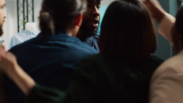 Clients shoving each other out of way to be first in clothing store during black friday shopping. African american guard holding back aggressive crowd breaking inside mall. Handheld shot.