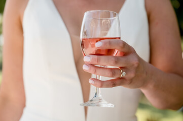 Bride in an elegant wedding gown holding a glass of rosé in her hand. Engagement ring visible. 