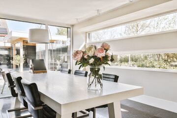 some flowers in a vase on a dining room table with chairs and a large window looking out to the backyard