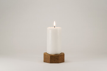 A lighted white wax candle burning isolated on white background and wooden stand with low light...