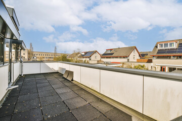 an outside area with houses in the background and blue sky above, as seen from a rooftop on a sunny...