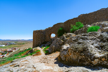 Pared de piedra medieval con un agujero y molinos de viento medievales al otro lado, desde Molinos...