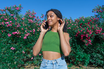 Young girl using her smartphone in the park on a sunny day with blue sky, greenery and flowers.