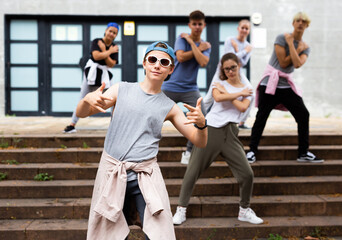 Fototapeta premium Positive teen boy dancing modern street dance outdoors with teenagers in background.