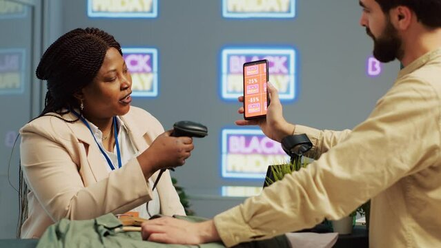Customer uses mobile loyalty program app at checkout counter in department store. Male shopper buying clothes in mall outlet center using black friday discounted voucher. Handheld shot.