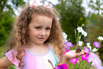 little cute curly girl holding colorful butterfly on hand. active childhood in summer. kid and...