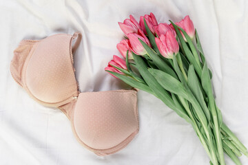 Gentle white lace bra on the bed with tulips. Women tender lingerie, underwear. Top view, close up. Flat lay, beauty blog or social media minimal concept. Present for Valentines, Women’s day