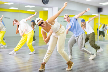 Emotional teenage girl having group dance training in studio, performing dynamic elements