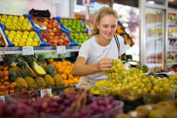 Fifteen-year-old girl who came to the supermarket for shopping chooses ripe grapes, putting the bunches in a package