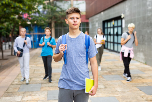 Focused teenager walking outside college building in autumn day, going to lessons.