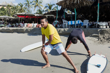 latin surf instructor and two men beginner surfers try to stand up on surfboard on lesson at beach...