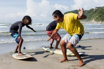latin surf instructor and two men beginner surfers try to stand up on surfboard on lesson at beach in Acapulco Mexico Latin America, Hispanic people surfing in summer sport activity