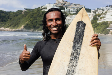 Portrait of surfer latin man with surf board on the beach in Acapulco Mexico. Hispanic people in...