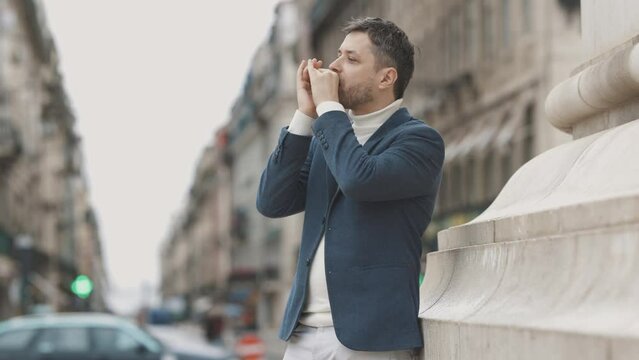 Man in jacket play harmonica on street during rain