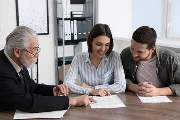 Young couple consulting insurance agent about pension plan at wooden table indoors