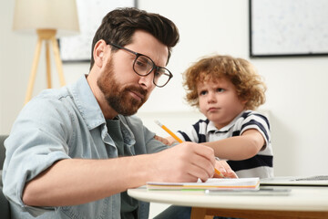 Little boy bothering his father at home. Man working remotely at desk