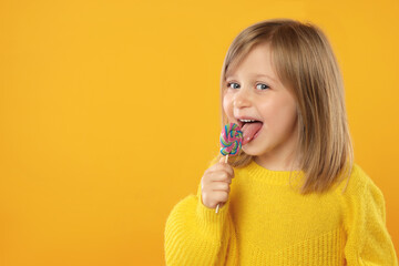 Portrait of cute girl licking lollipop on orange background, space for text