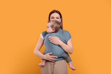 Mother holding her child in baby wrap on orange background
