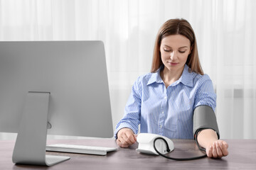 Woman measuring blood pressure at wooden table in room