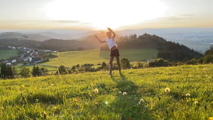 Little girl doing Cartwheel gymnastics sideways rotary movement on green grass hills at sunset time near Zilina town in Slovakia. Happy childhood moments or outdoor time spending concept 4K footage.