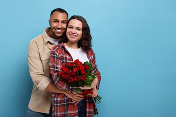 Happy couple celebrating Valentine's day. Beloved woman with bouquet of red roses on light blue background. Space for text