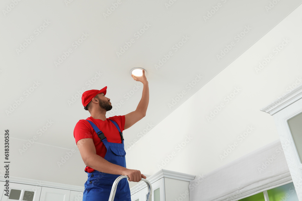 Poster Electrician repairing ceiling lamp indoors, low angle view. Space for text