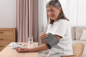 Woman measuring blood pressure at wooden table in room, space for text