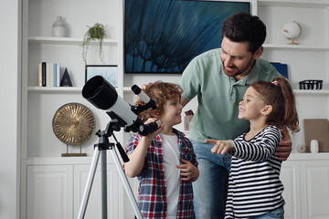 Happy father and children using telescope to look at stars in room