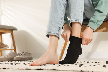 Woman putting on black socks at home, closeup