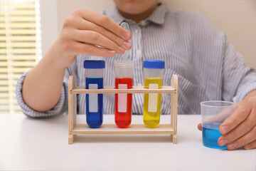 Girl with colorful liquids in test tubes and beaker at white table indoors, closeup. Chemical experiment set for kids