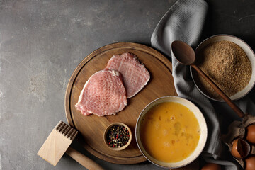 Ingredients for cooking schnitzel and meat tenderizer on grey textured table, flat lay. Space for...