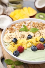 Tasty matcha smoothie bowl served with fresh fruits and oatmeal on table, closeup. Healthy breakfast