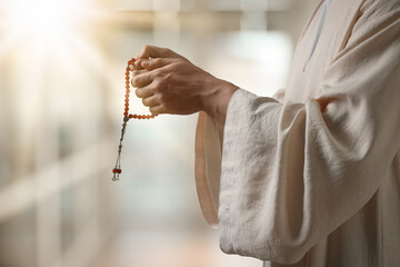 Muslim man with misbaha praying on blurred background, closeup