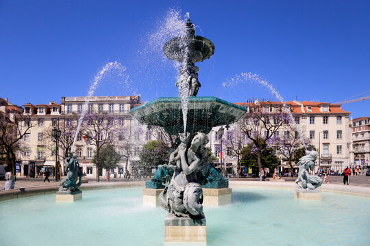 A majestosa fonte monumental na Pra&ccedil;a do Rossio, em Lisboa, brilha sob o sol e o c&eacute;u azul.