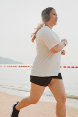 chubby woman wearing sport wear and haedphone running on sea beach with happiness