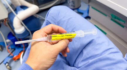 hand holds a syringe amidst IV drips and medications, symbolizing medical care, treatment, and the use of drugs in a hospital setting