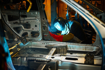 Worker in mask welds metal parts of auto carcass in shop