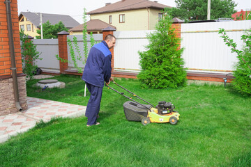 The man is working in the garden. Mowing grass with a lawn mower.