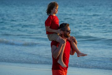Outdoor portrait of happy father and son walking on sunny ocean beach. Father and son walk in sea...