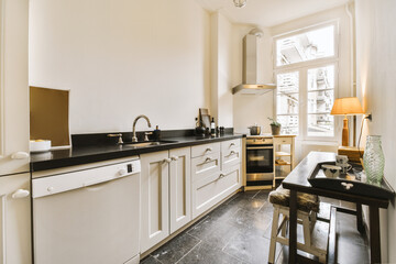 a small kitchen with white cabinets and black counter tops on the island in front of the sink is next to the window